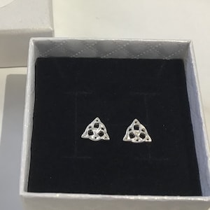 May include: A pair of silver earrings featuring a triangular Celtic knot design. The earrings are presented in a small white box with a black velvet lining.