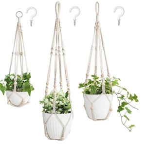 May include: Three macrame plant hangers with white pots and green plants. Each hanger has wooden beads and is attached to a white hook.