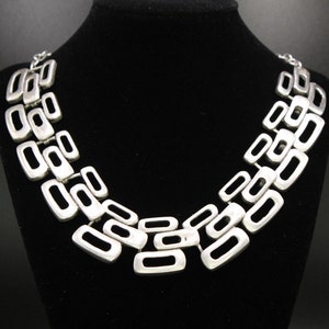 May include: A silver necklace with a geometric design featuring interlocking rectangular links.