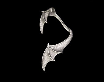 May include: Silver-toned metal ring with a bat wing design. The ring is open and can be adjusted to fit different finger sizes.