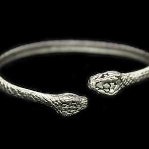 May include: Silver snake bangle bracelet with two snake heads facing opposite directions.