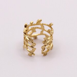 May include: Gold ring with a delicate, openwork design featuring a repeating leaf pattern. The ring is adjustable and has a slightly curved shape.