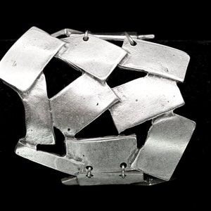 May include: A silver bracelet made of interlocking, geometric shapes. The bracelet is open and has a hinged clasp.