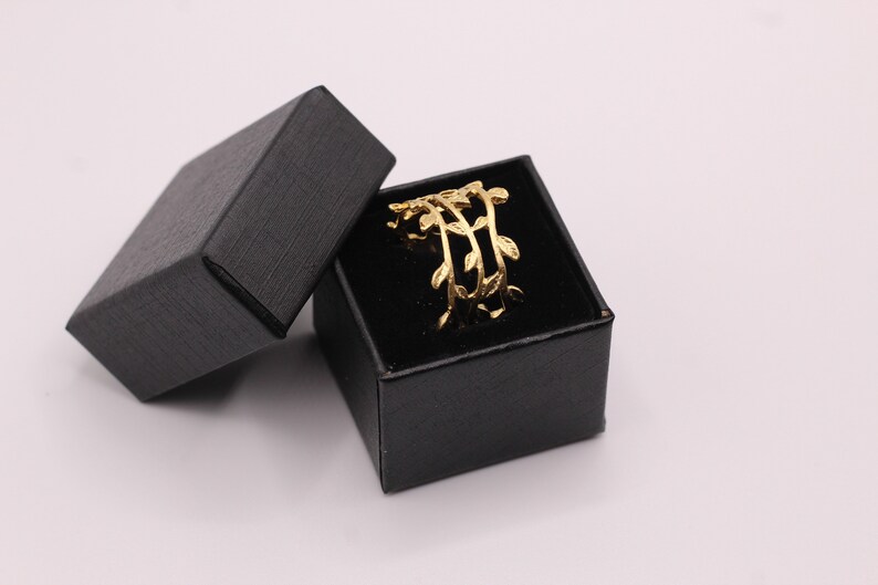 May include: A gold ring with a delicate leaf design, displayed in a black velvet ring box.