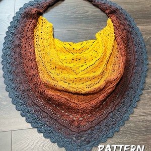 May include: A crocheted shawl with a gradient of colors from dark blue to brown to yellow. The shawl has a scalloped edge and a delicate lace pattern.