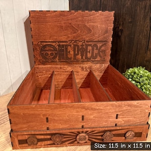 May include: A wooden storage box with a hinged lid, featuring the "ONE PIECE" logo and character art. The box is 11.5 inches x 11.5 inches x 4.5 inches and has internal dividers. The box is made of stained wood with a sunburst design.