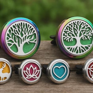 Op de afbeelding: Een verzameling auto-luchtroosterverspreiders met verschillende ontwerpen. Twee grotere diffusers hebben een levensboomontwerp met groene en zilveren accenten. Kleinere diffusers tonen een hert, lotusbloem, hart en pentagram. De diffusers hebben een metallic afwerking.