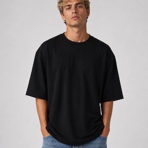 May include: A black, oversized t-shirt with short sleeves. The shirt is made of a soft material and is being worn with blue jeans. The model is standing in front of a plain, light gray background.