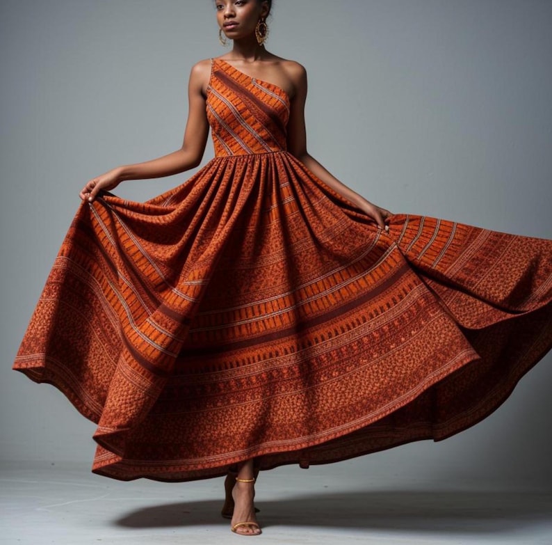 May include: A one-shoulder, floor-length dress with a rust-colored, patterned fabric. The dress has a fitted bodice and a flowing skirt.