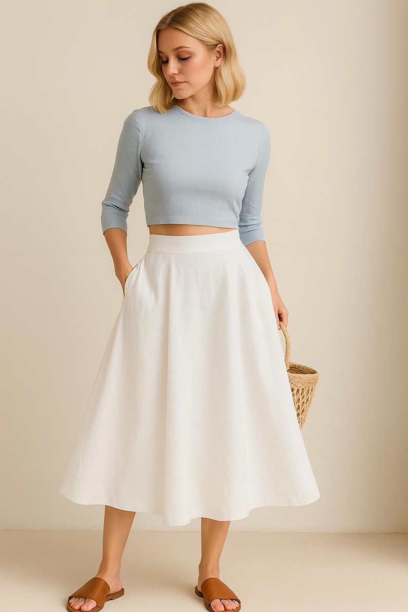 Puede incluir: Un top corto azul claro de manga tres cuartos combinado con una falda midi blanca. La falda tiene cintura alta y bolsillos. Sandalias de cuero marr&oacute;n y una cesta de mimbre completan el conjunto.