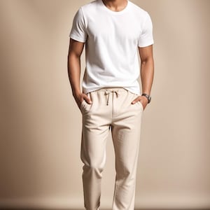 May include: A person wearing a white crew neck t-shirt, beige drawstring pants, and white sneakers. The outfit is simple and casual, suitable for everyday wear. The background is a solid beige color.