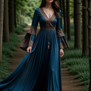 Op de afbeelding: Een teal maxi-jurk met lange mouwen en een V-hals. De jurk heeft een bruine geborduurde rand rond de halslijn en manchetten. De jurk is getailleerd met een bruine riem en heeft een kwast die aan de riem hangt.