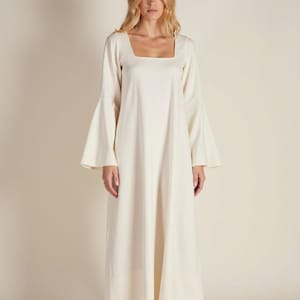 May include: A long, white maxi dress with a square neckline and long, wide bell sleeves. The dress is made from a lightweight fabric and has a flowing silhouette.