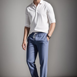 May include: A white polo shirt with long sleeves and blue pants. The pants have a drawstring waist and are cuffed at the ankles. White sneakers complete the outfit. The man is wearing a watch.