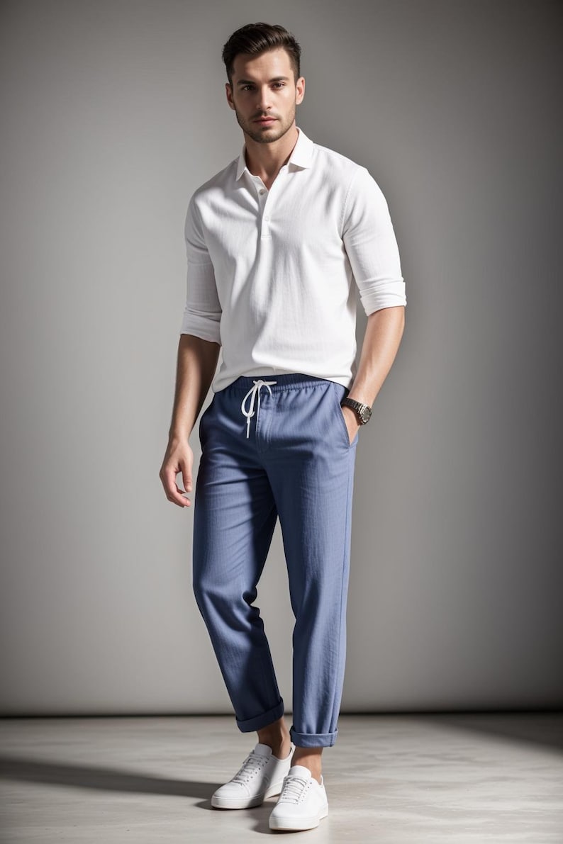 May include: A white polo shirt with long sleeves and blue pants. The pants have a drawstring waist and are cuffed at the ankles. White sneakers complete the outfit. The man is wearing a watch.