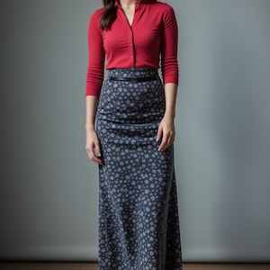 May include: A woman wearing a red long-sleeved shirt and a long, gray floral skirt with a black belt. She is wearing black ankle boots.