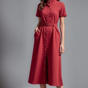 Pode incluir: Um vestido camisa vermelho midi com fecho de botões, mangas curtas e cinto na cintura.