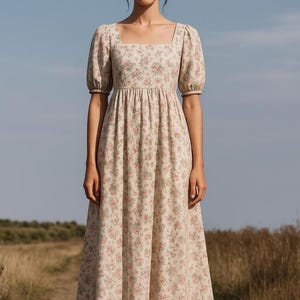 K&ouml;nnte beinhalten: Beige gebl&uuml;mtes Kleid mit quadratischem Ausschnitt und kurzen Puff&auml;rmeln. Das Kleid hat ein eng anliegendes Oberteil und einen flie&szlig;enden Rock. Es ist mit kleinen rosa Blumen verziert.