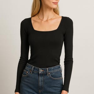 May include: A black long-sleeve top with a square neckline and ribbed texture. The top is paired with blue denim jeans. The model is wearing a gold necklace.