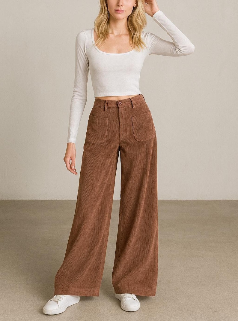 May include: A woman wearing a white long-sleeve scoop neck crop top and brown corduroy wide-leg pants. The pants have two front pockets and are paired with white sneakers.