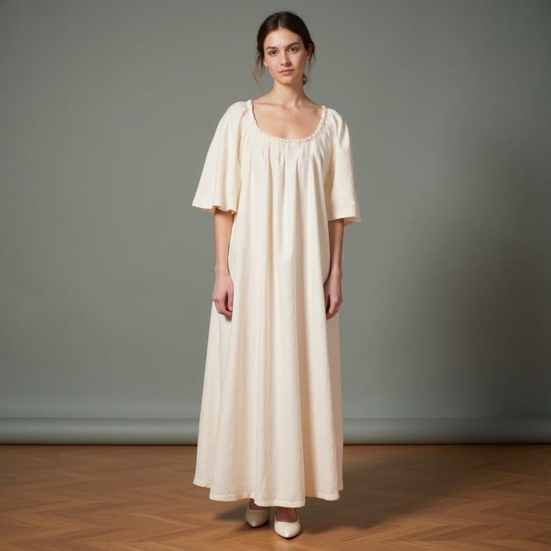 May include: A long, white, cotton dress with a scoop neck and short sleeves. The dress has a gathered waist and a flowing skirt.