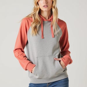 May include: A gray and coral colored hooded sweatshirt with a kangaroo pocket. The sweatshirt has a contrasting color on the sleeves and a drawstring hood.