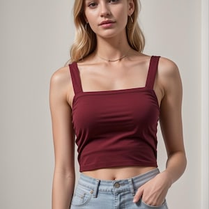 May include: A woman wearing a burgundy square neck crop top with thin straps and light blue jeans.