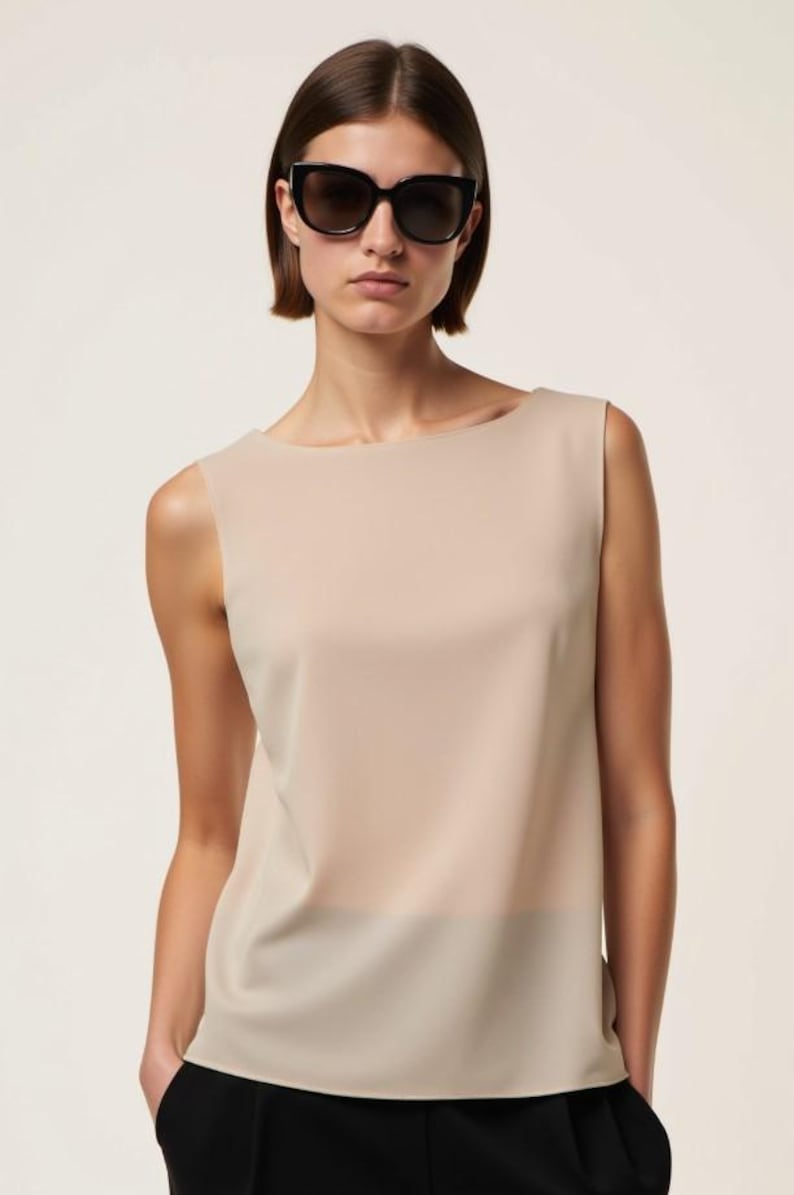 May include: A woman wearing a beige sleeveless top with a scoop neck and black sunglasses.