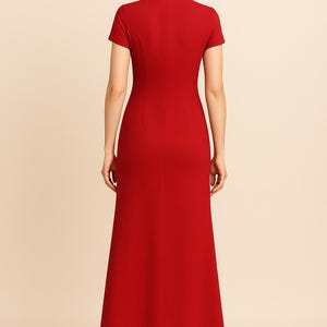 May include: A floor-length, red dress with a high neckline and short sleeves. The dress has a fitted bodice and a flared skirt. The back of the dress is visible, showing a vertical seam. The model is wearing the dress.