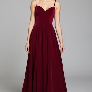 May include: A long, burgundy velvet dress with a sweetheart neckline and thin straps. The dress has a fitted bodice and a flowing skirt.