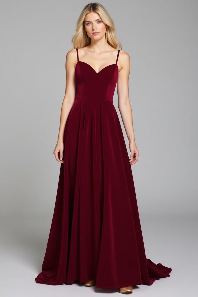 May include: A long, burgundy velvet dress with a sweetheart neckline and thin straps. The dress has a fitted bodice and a flowing skirt.