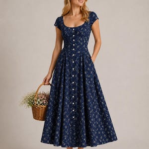 K&ouml;nnte beinhalten: Ein marineblaues Midikleid mit wei&szlig;em Blumenmuster, Rundhalsausschnitt, kurzen &Auml;rmeln und einem ausgestellten Rock mit durchgehender Knopfleiste vorne. Das Kleid verf&uuml;gt &uuml;ber Seitentaschen und wird mit einem kleinen geflochtenen Weidenkorb kombiniert.