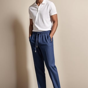 May include: A man wearing a white polo shirt and navy blue drawstring pants. The outfit is completed with white sneakers. The clothing is casual and suitable for warm weather.