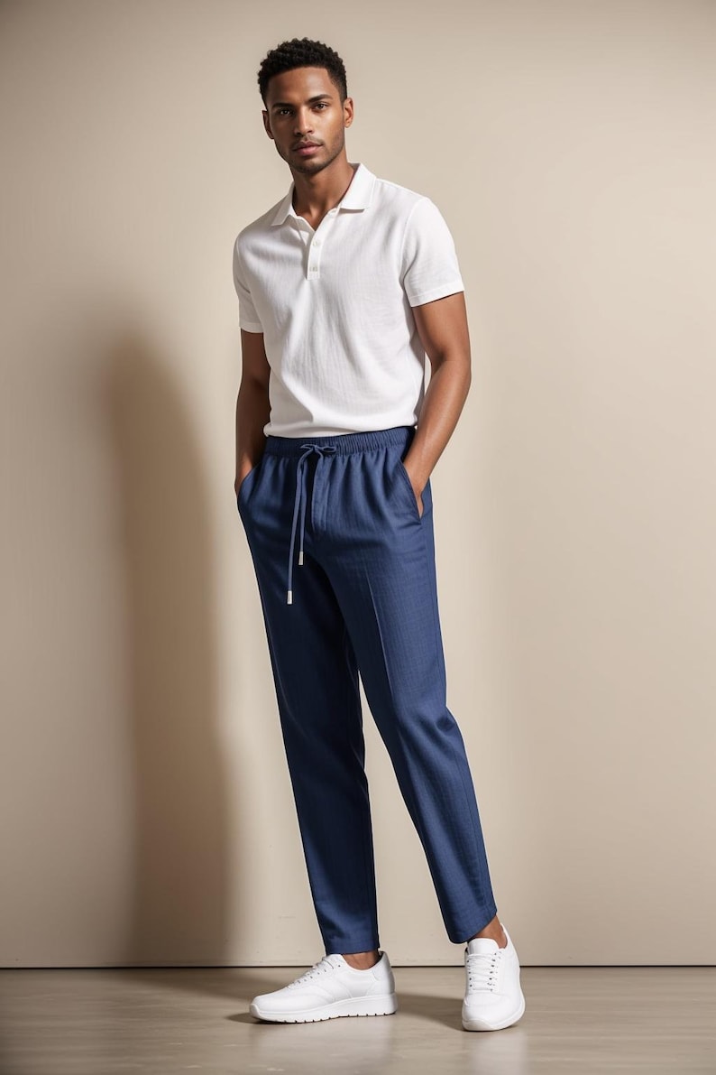 May include: A man wearing a white polo shirt and navy blue drawstring pants. The outfit is completed with white sneakers. The clothing is casual and suitable for warm weather.