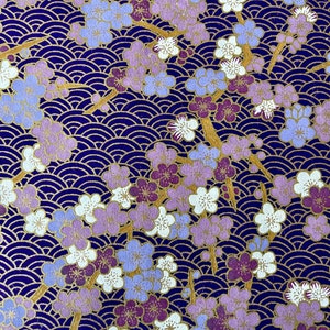 May include: A close-up of a purple and gold patterned fabric with a repeating design of flowers and waves. The fabric has a textured surface and a subtle sheen.