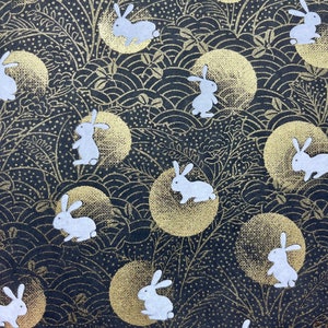 May include: A black background with a repeating pattern of white rabbits and gold circles. The rabbits are in various poses and the circles have a textured look.
