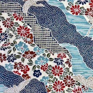 May include: A white fabric with a blue and white wave pattern and a red, white and green floral pattern. The fabric features white cranes flying over the waves.
