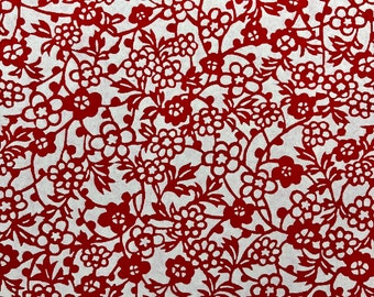 May include: Red paper with a delicate floral pattern cut out of it. The pattern features small flowers and leaves, creating a intricate design.