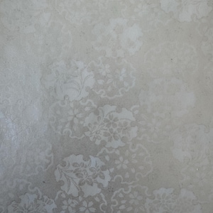May include: A close-up of a textured surface with a repeating floral pattern in shades of white and gray. The design features stylized flowers and leaves arranged in circular clusters, creating a subtle, elegant aesthetic.