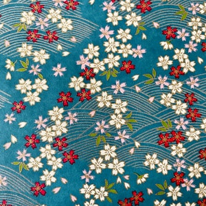 May include: A teal blue fabric with a repeating pattern of white and gold flowers with red accents. The background has a subtle wave pattern.