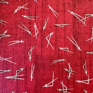 May include: Close-up of a red fabric with a textured appearance. The fabric is covered with a pattern of white, arrow-like shapes pointing in various directions. The arrows have a simple, geometric design.