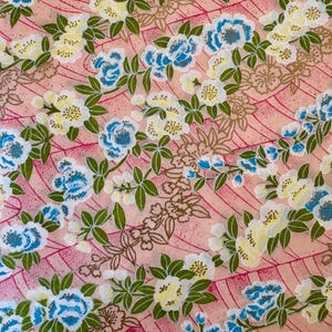 May include: A pink fabric with a repeating pattern of white and blue flowers with green leaves. The background has a pink and white striped pattern.