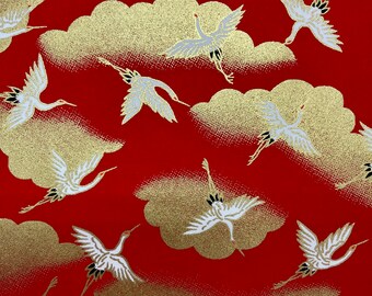 May include: Red fabric with a repeating pattern of white cranes flying over gold clouds. The cranes have black accents on their wings and heads.