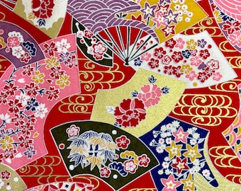 May include: A red fabric with a repeating pattern of gold fans, flowers, and geometric shapes. The fans are decorated with pink, white, and blue flowers. The geometric shapes are red, white, and gold.
