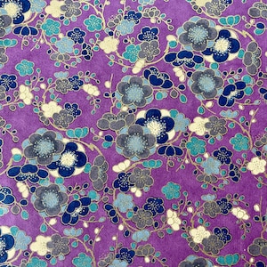 Könnte beinhalten: Lilafarbener Stoff mit einem sich wiederholenden Muster aus goldenen, blauen und weißen Blumen. Die Blumen sind stilisiert und haben ein traditionelles japanisches Design.