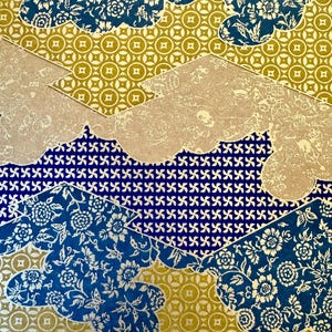 May include: A patterned design featuring overlapping shapes with floral and geometric patterns. The design incorporates blue, gold, and beige colors. The blue sections have white floral designs, while the gold sections have a circular pattern.