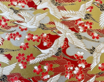 May include: Red and gold patterned wrapping paper with white cranes flying in a repeating pattern. The paper is decorated with red and white cherry blossoms.