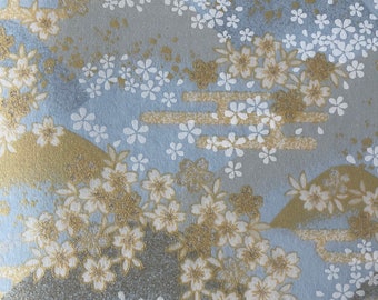 May include: A blue and gold fabric with a repeating pattern of white flowers and stylized mountains. The fabric has a subtle glitter finish.