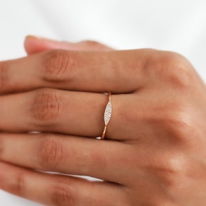 May include: A delicate gold ring with a small, oval-shaped diamond setting. The ring is worn on the finger of a hand.