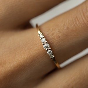 Pode incluir: Um delicado anel de banda de ouro com cinco pequenos diamantes engastados em uma linha curva.